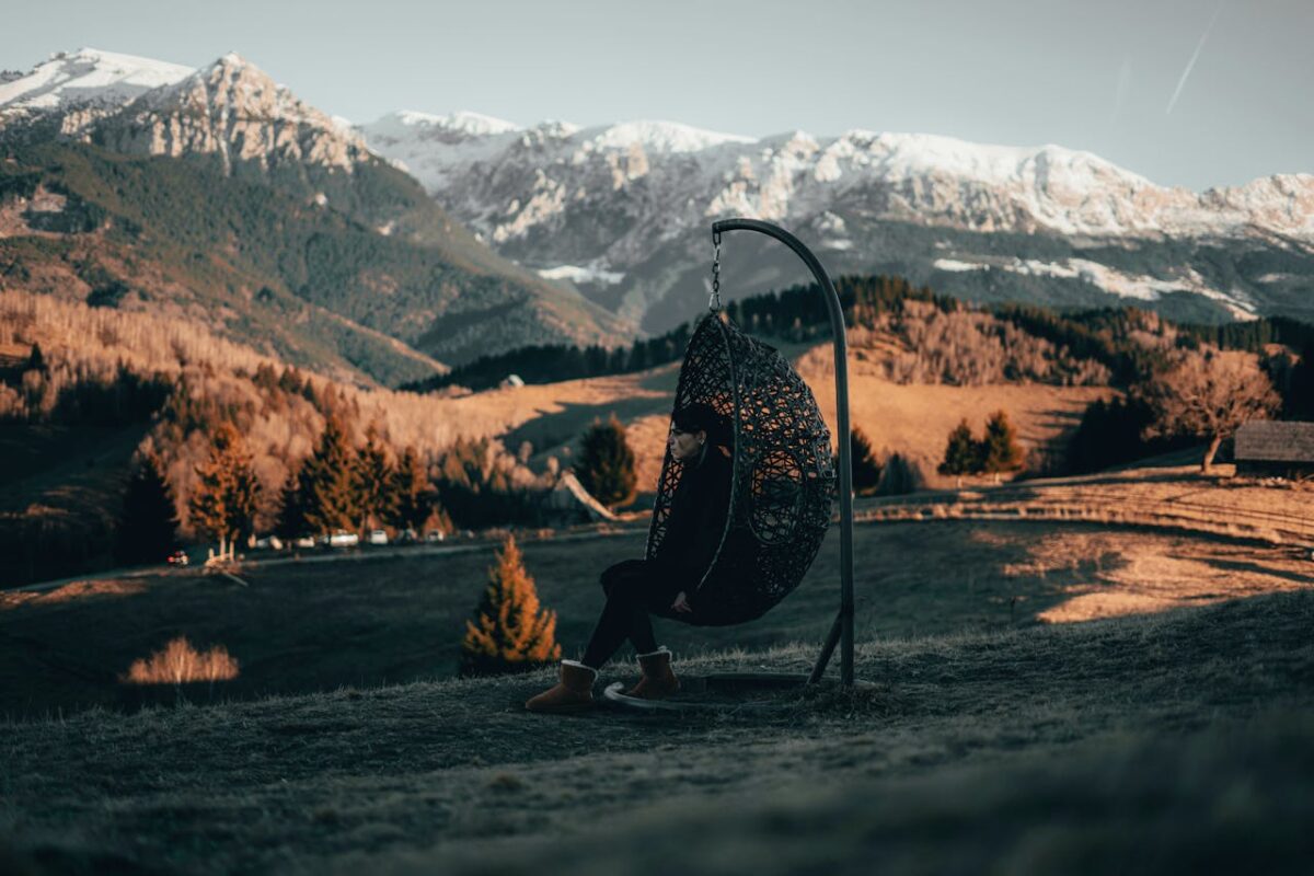 Young woman sitting in a swing chair overlooking a stunning mountain landscape during sunset.