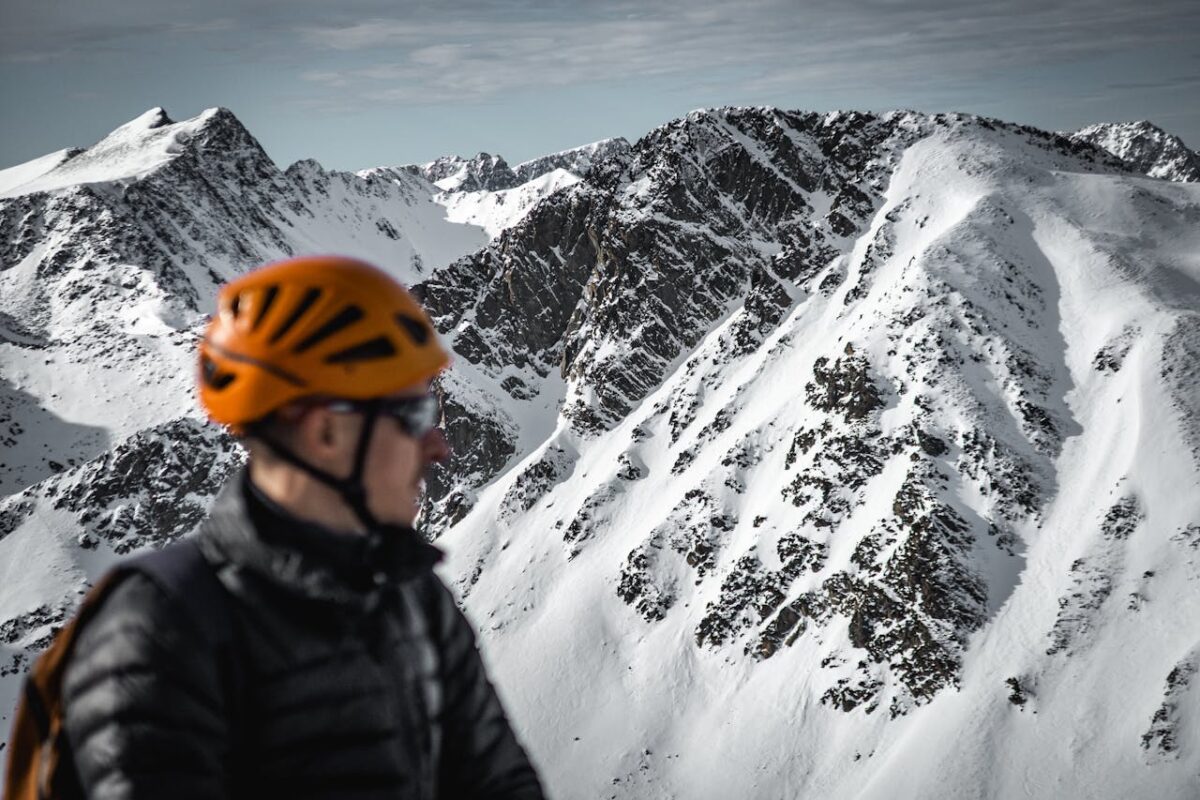 A man wearing an orange helmet gazes at a scenic snow-covered mountain range, embodying adventure and exploration.