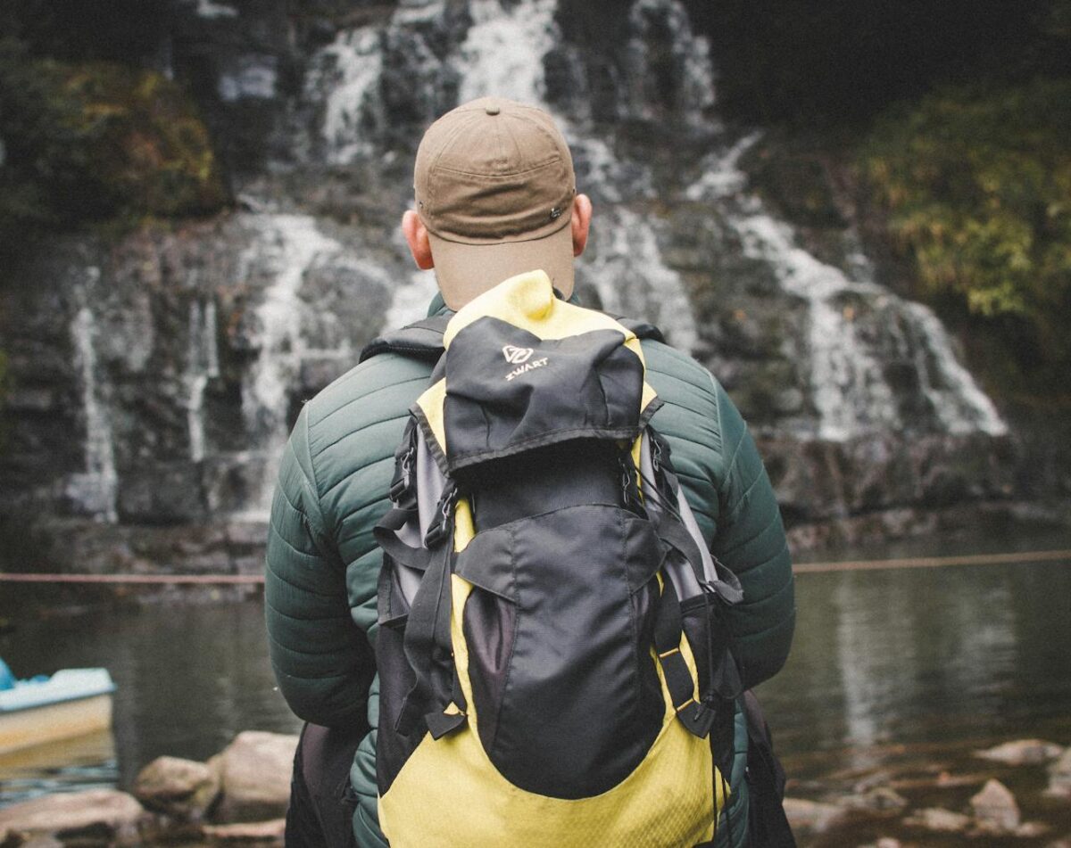 A man with a backpack admires a waterfall, reflecting adventure travel.